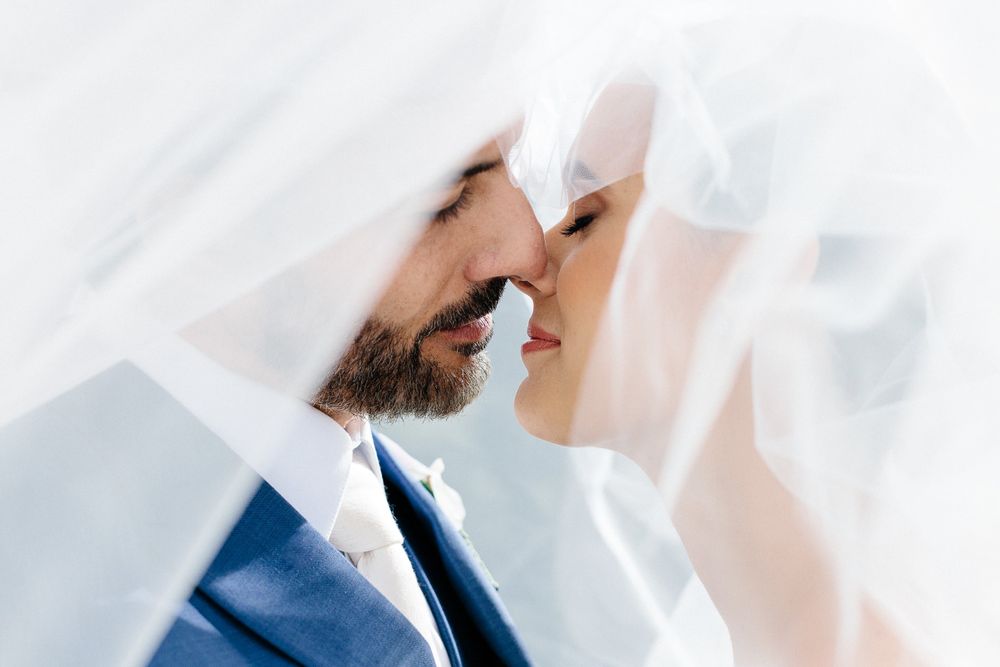 Intimate close-up portrait of newlyweds sharing a tender moment under a veil.