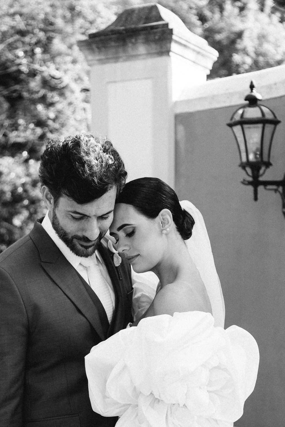 Intimate black and white portrait of newlyweds sharing a tender moment against a white wall.