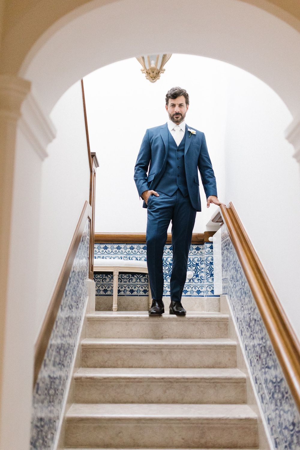 Man in blue suit standing on tiled staircase under an arched doorway.