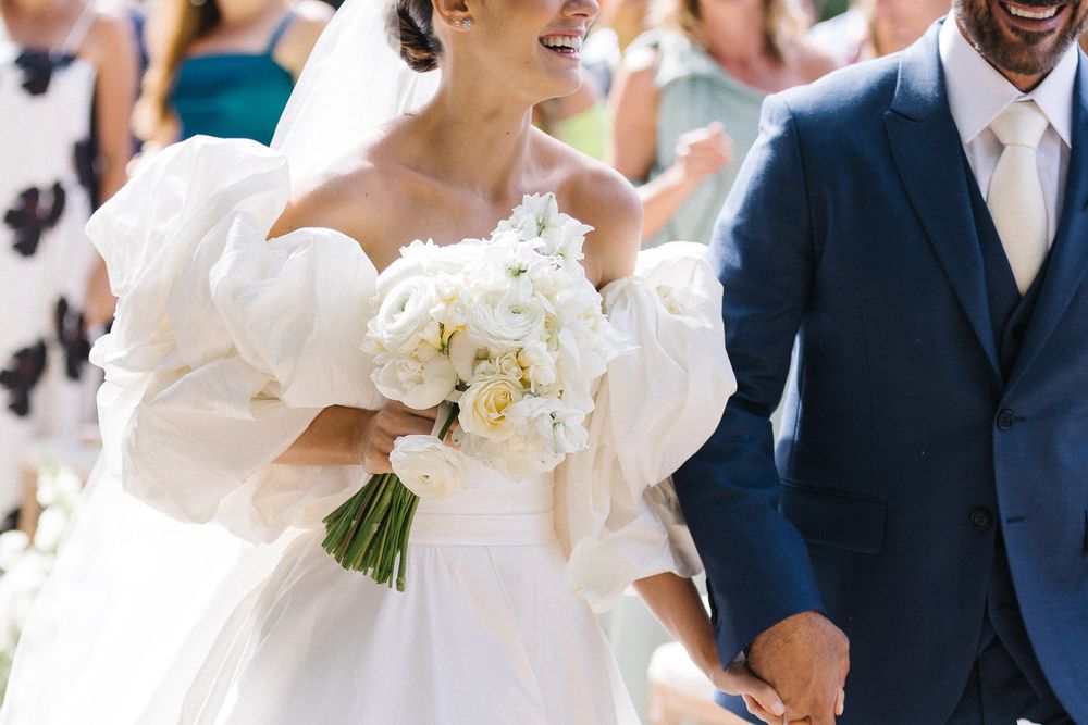 Elegant bride in a white dress holds a beautiful bouquet of white flowers while walking outdoors.
