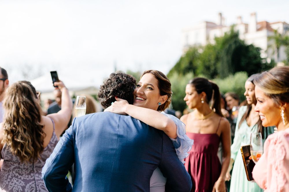 Joyful outdoor wedding celebration with guests hugging and taking photos.
