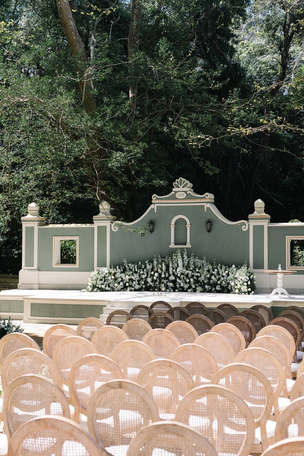 Outdoor wedding ceremony setup with wooden chairs facing an ornate grey stone wall backdrop.