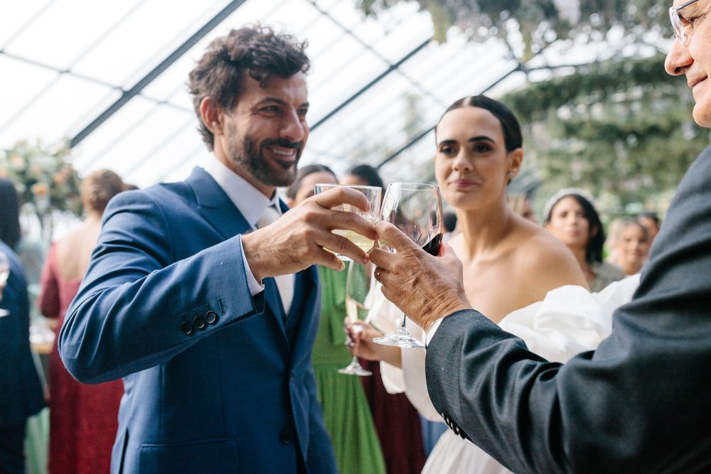 Wedding guests toasting with champagne glasses in a greenhouse reception venue.
