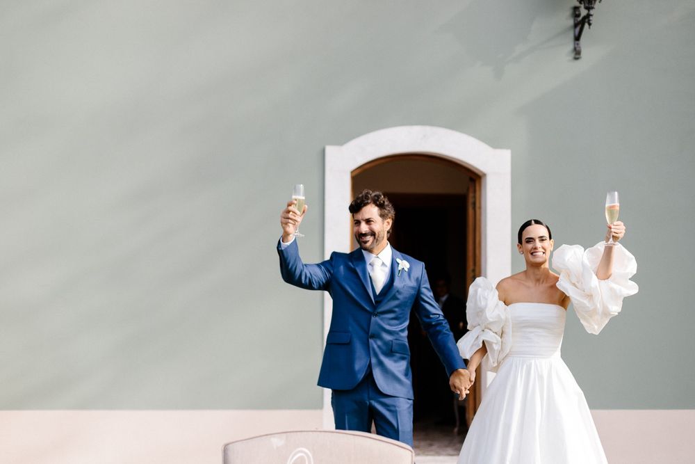 Newlyweds celebrate with champagne toast outside white stucco building.