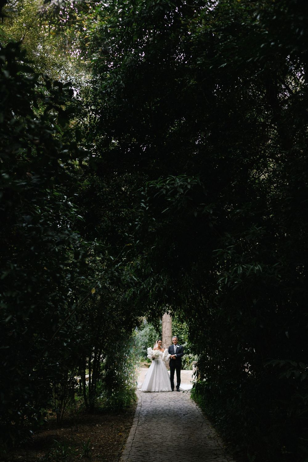 Romantic wedding photo framed by lush garden archway on stone path.