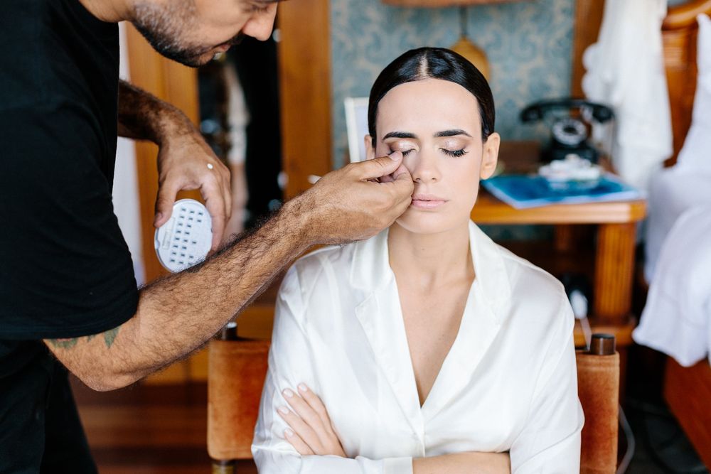 Professional makeup artist applying cosmetics to a client wearing a white robe in a salon setting.
