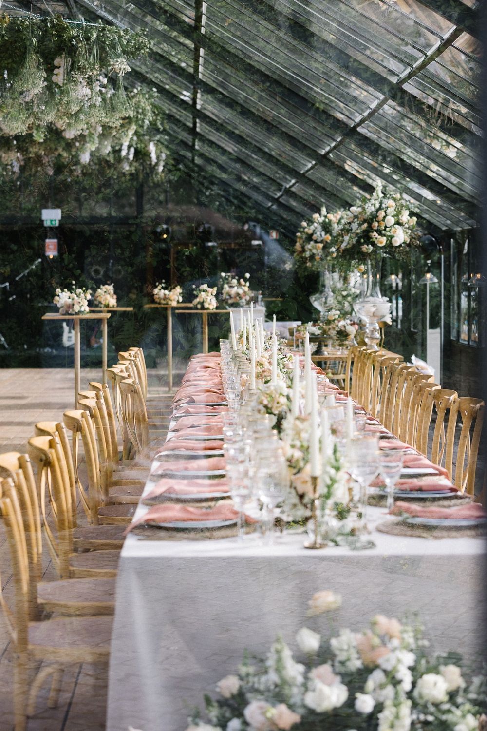 Elegant wedding reception table setting with gold chairs and floral centerpieces in greenhouse venue.