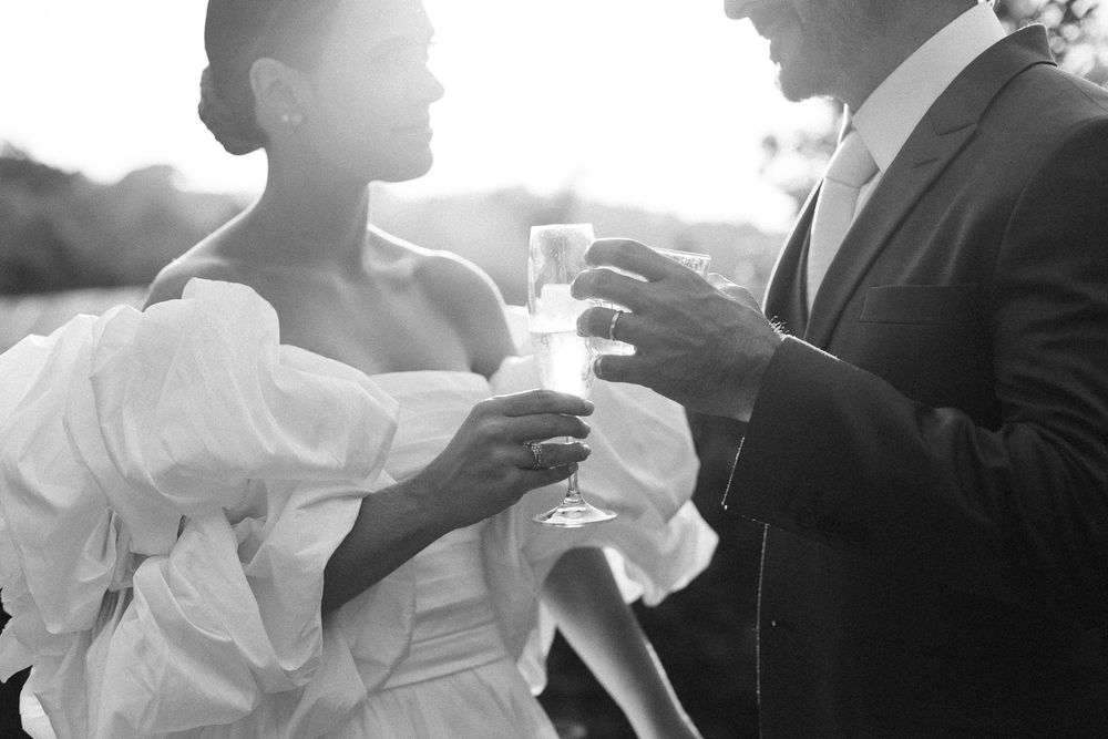 Black and white photo of newlyweds sharing drinks during an outdoor celebration.