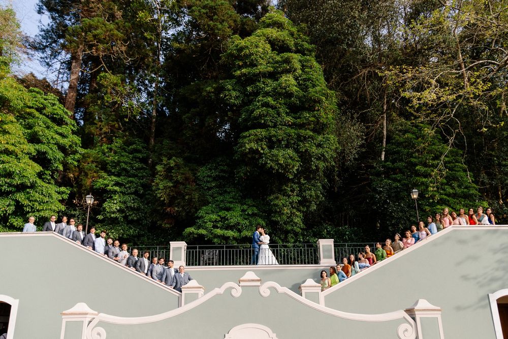 Wedding guests lined up along curved stone staircase surrounded by evergreen trees.