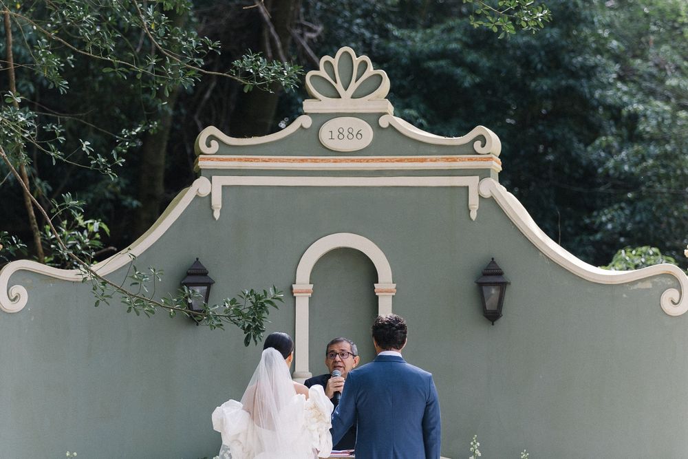 A wedding ceremony taking place under an elegant grey archway decorated with lanterns and ornamental details.