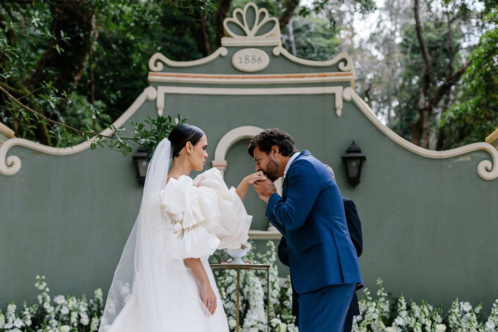An elegant outdoor wedding ceremony in front of an ornate grey wall with decorative architectural details.