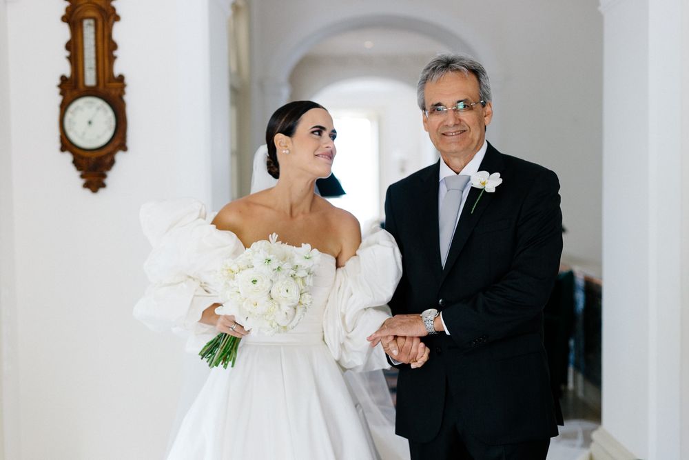 Elegant wedding moment in white hallway with ornate clock on wall.