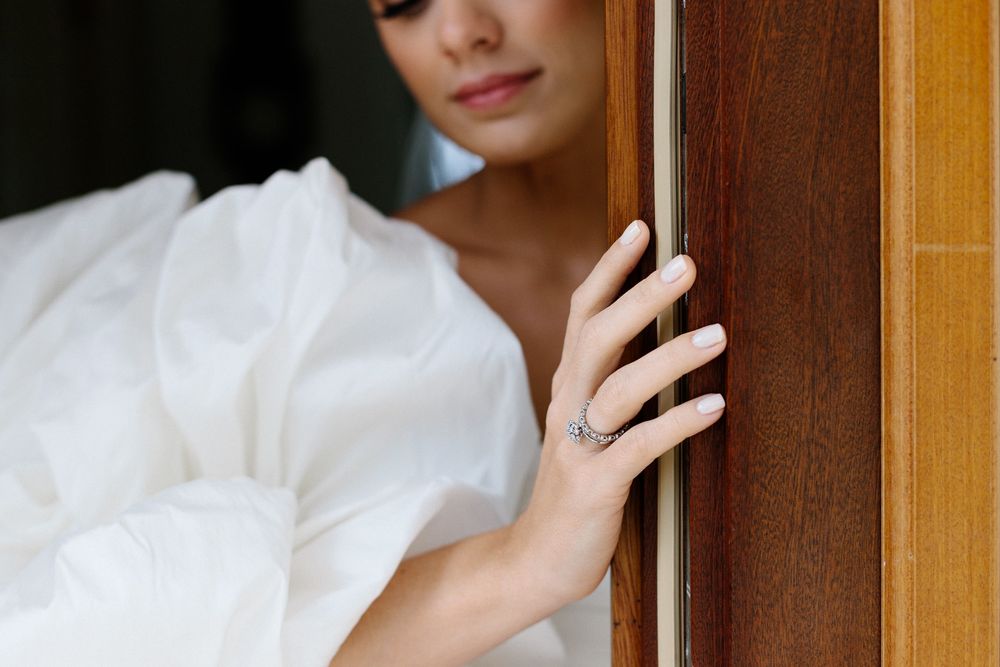 Close-up detail shot of hand on wooden door wearing elegant white bridal gown.