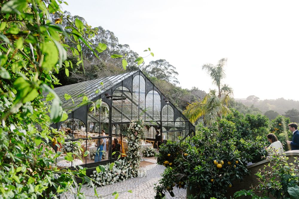 Exterior view of a glass greenhouse wedding venue surrounded by lush greenery.