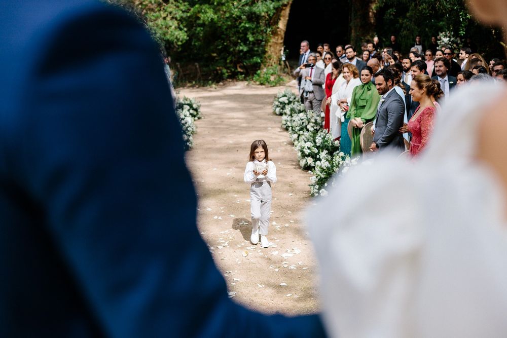 A young flower girl walks down an outdoor wedding aisle lined with guests and floral arrangements.