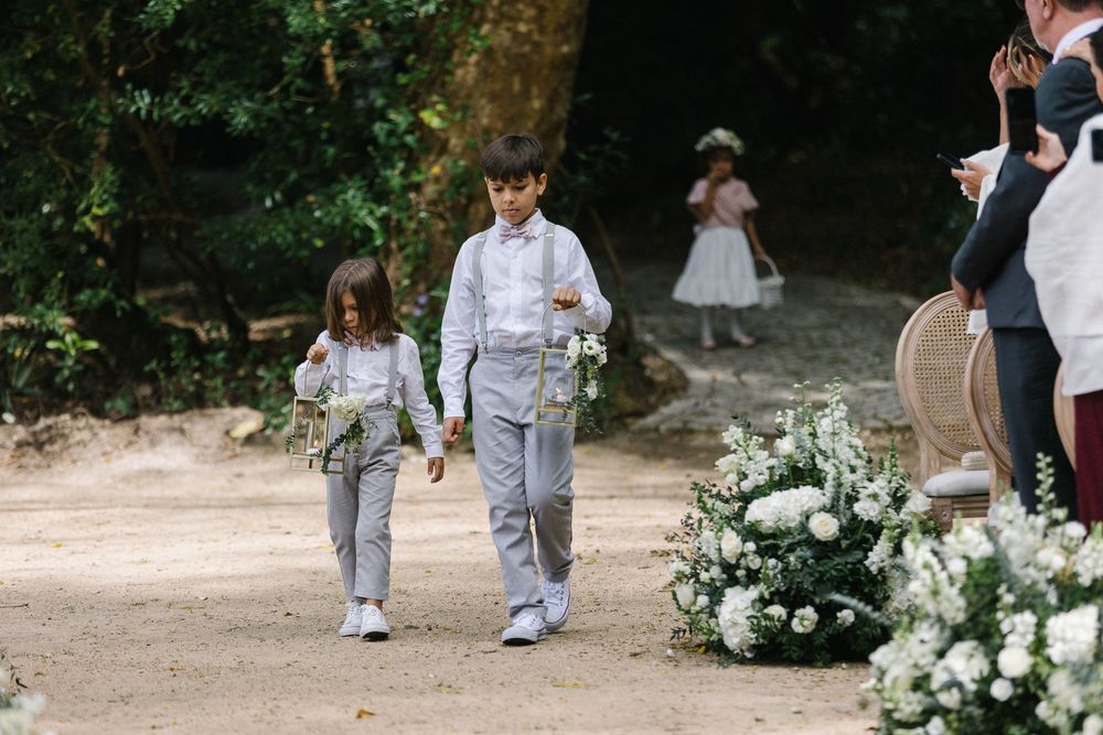 Children in matching outfits walking down a garden path lined with white floral arrangements.