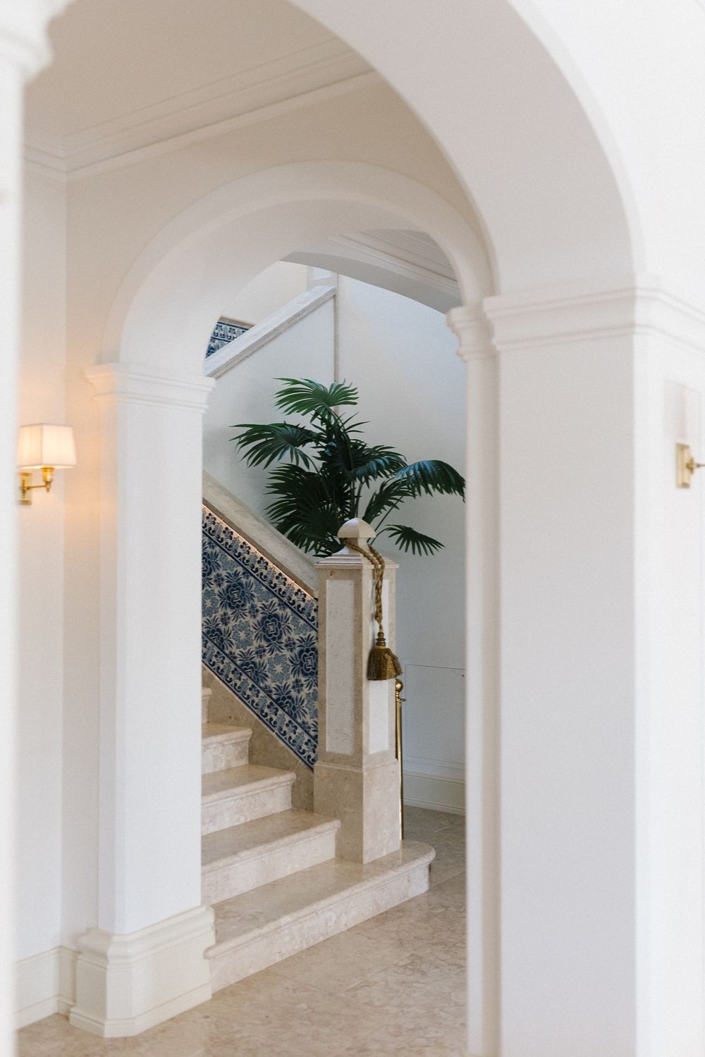 Elegant white archway with blue tile detail and palm plant leading to a grand staircase.