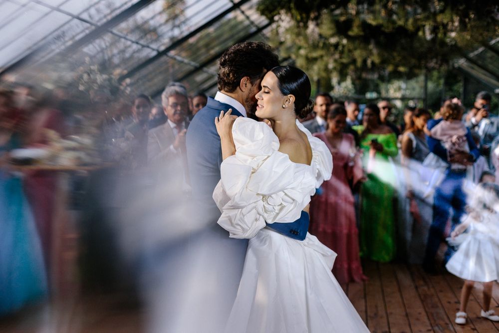 Wedding couple dancing surrounded by guests in a greenhouse venue.