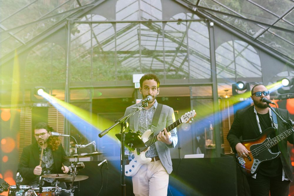 Live band performing with blue stage lights in a greenhouse venue.