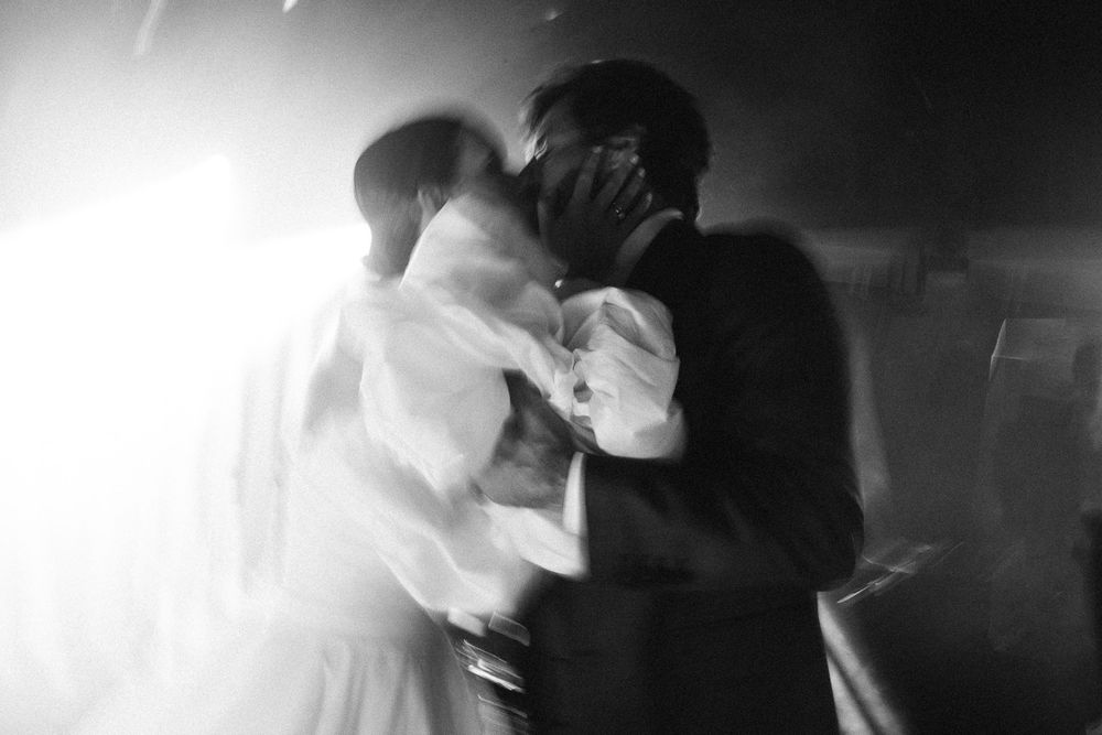A romantic black and white first dance moment at a wedding reception with dramatic backlighting.