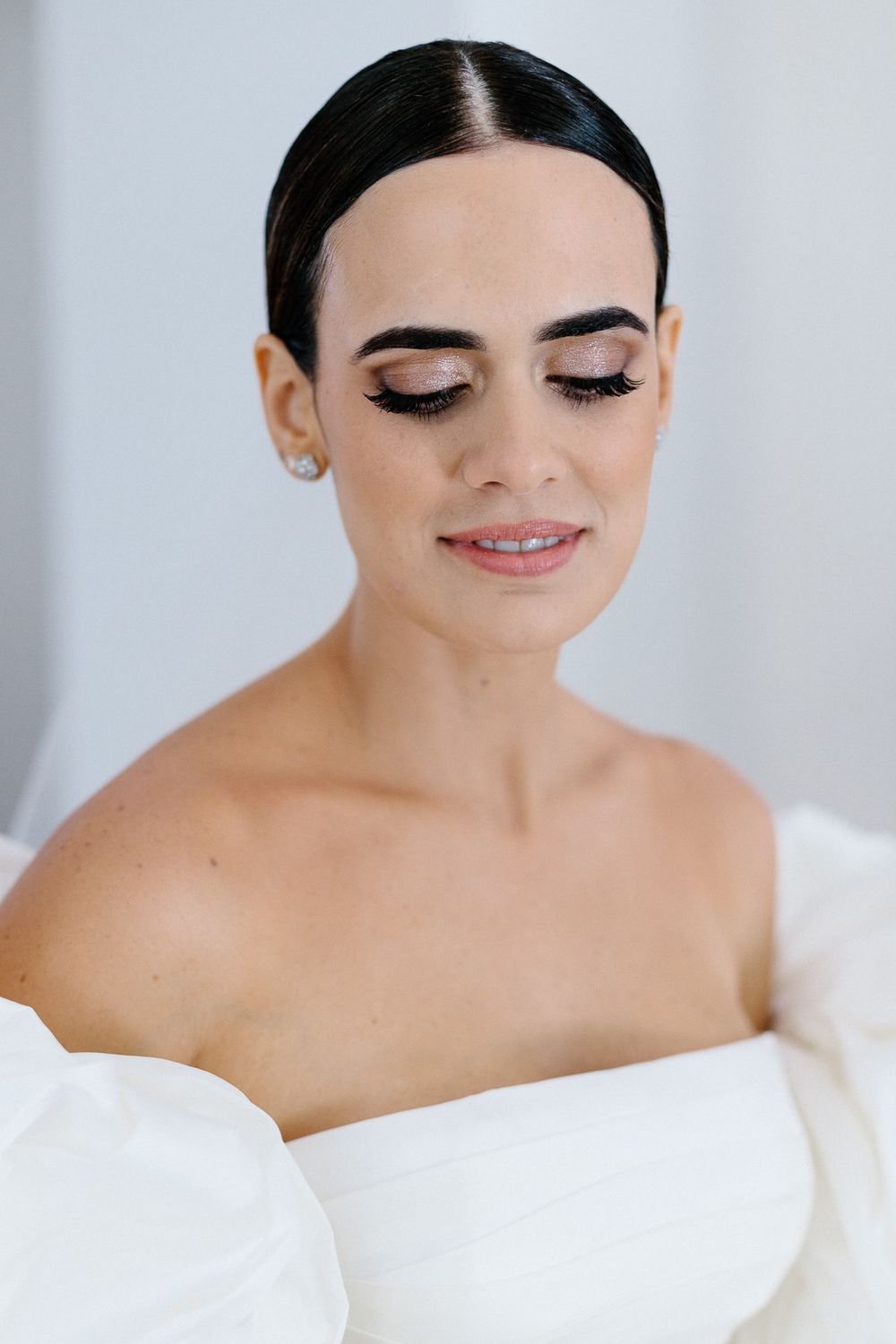 Bride wearing elegant off-shoulder wedding gown with natural makeup and sleek hairstyle.