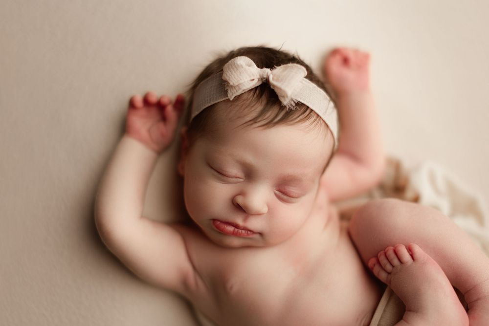 baby girl with a blush pink bow sleeping on back for her newborn session