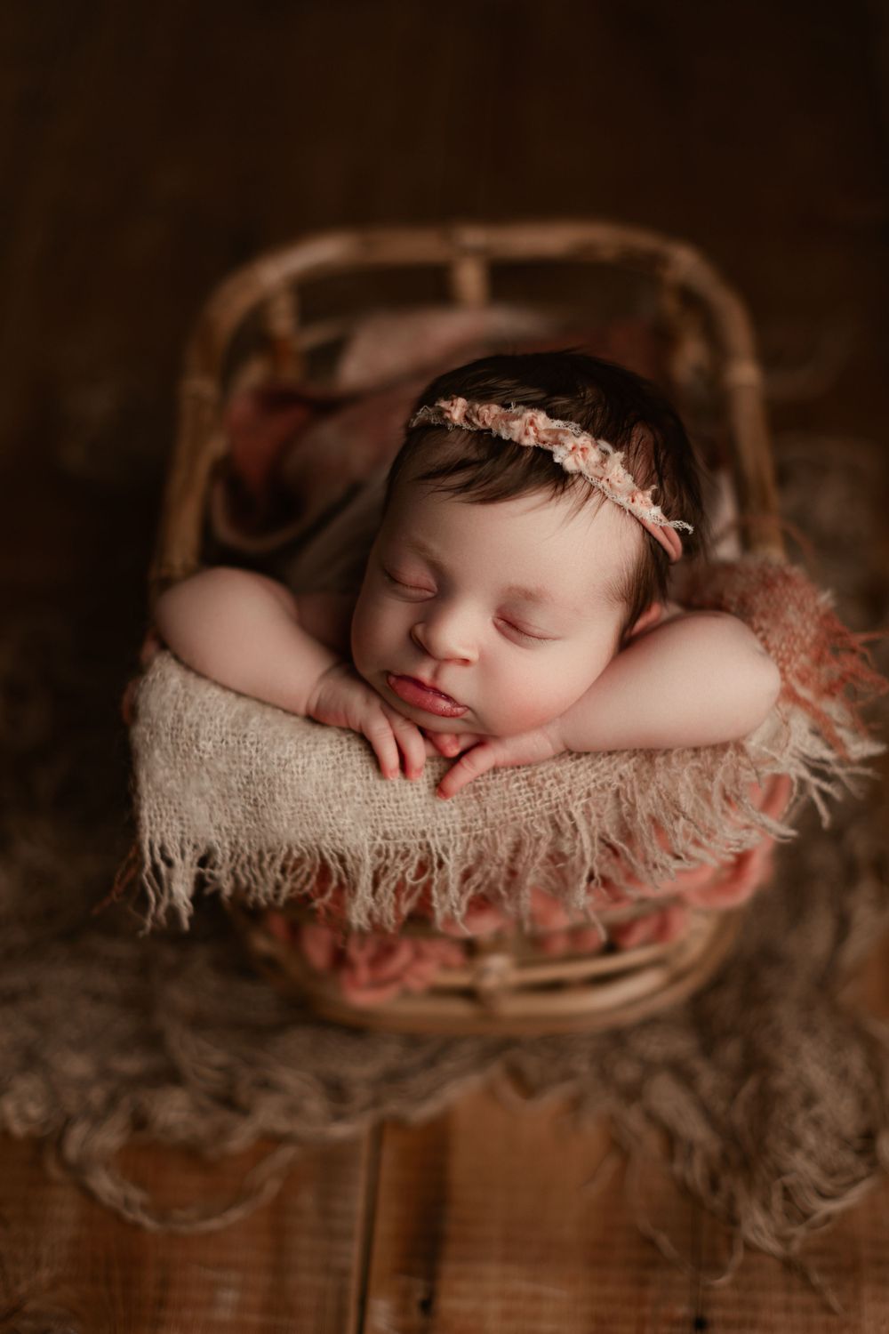 newborn girl with a pink headband posed in a bamboo newborn prop