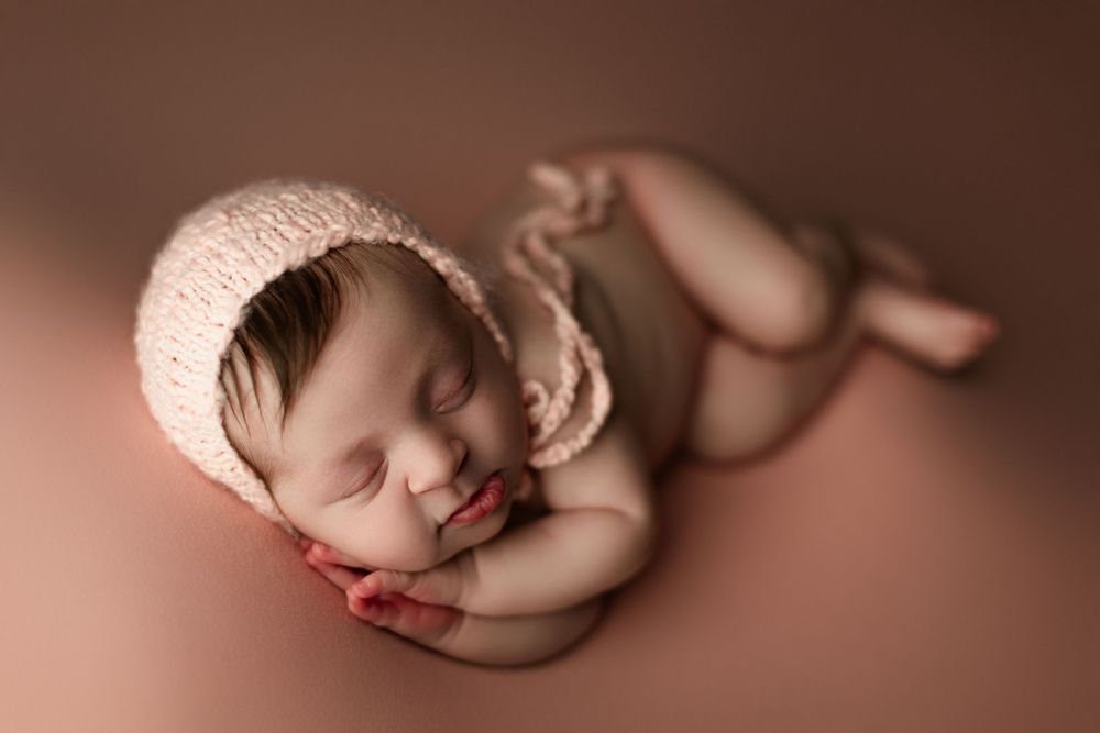 newborn girl on pink backdrop side laying pose