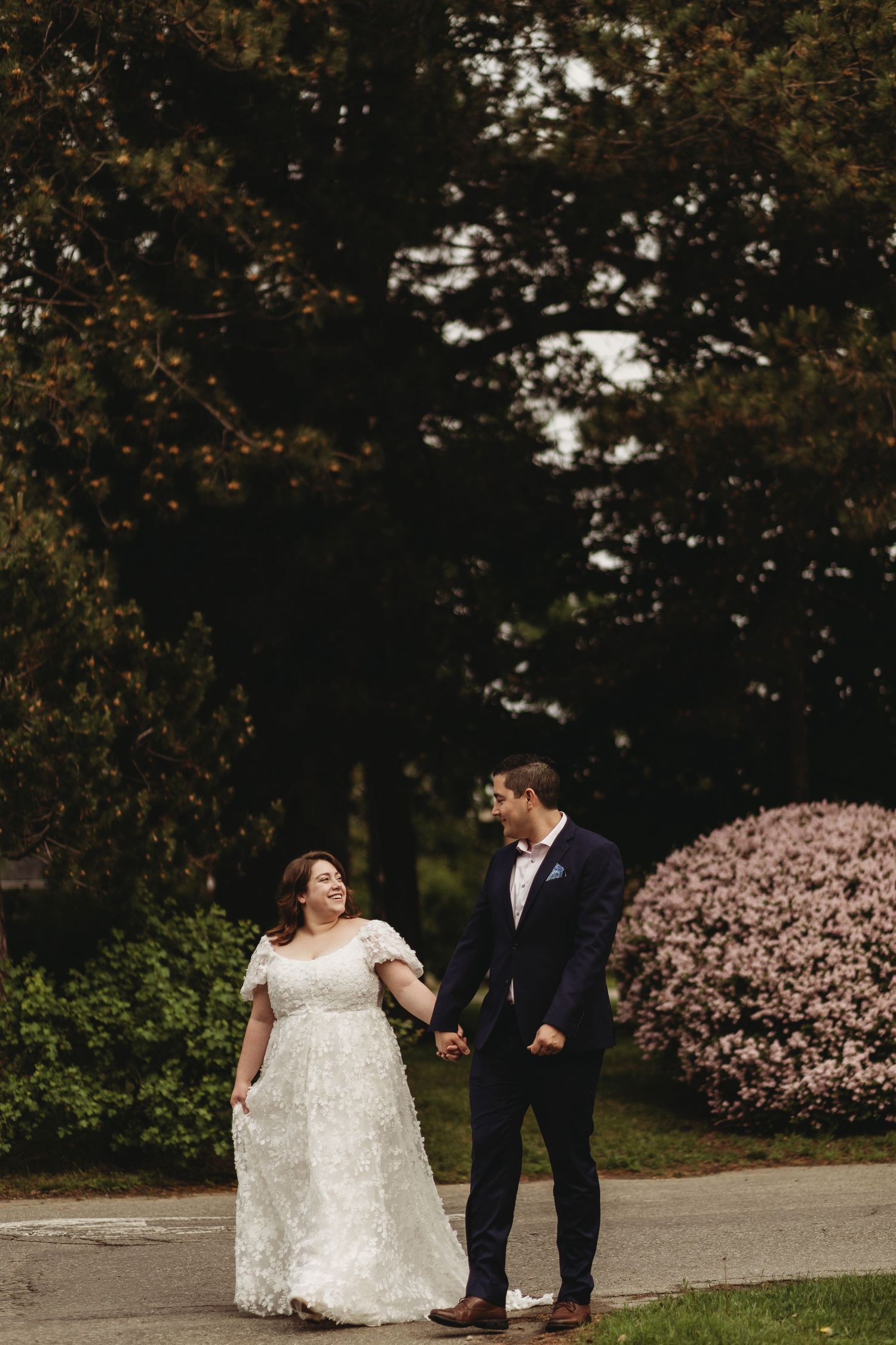 A couple walks hand in hand along a path with flowering spring trees in the background.