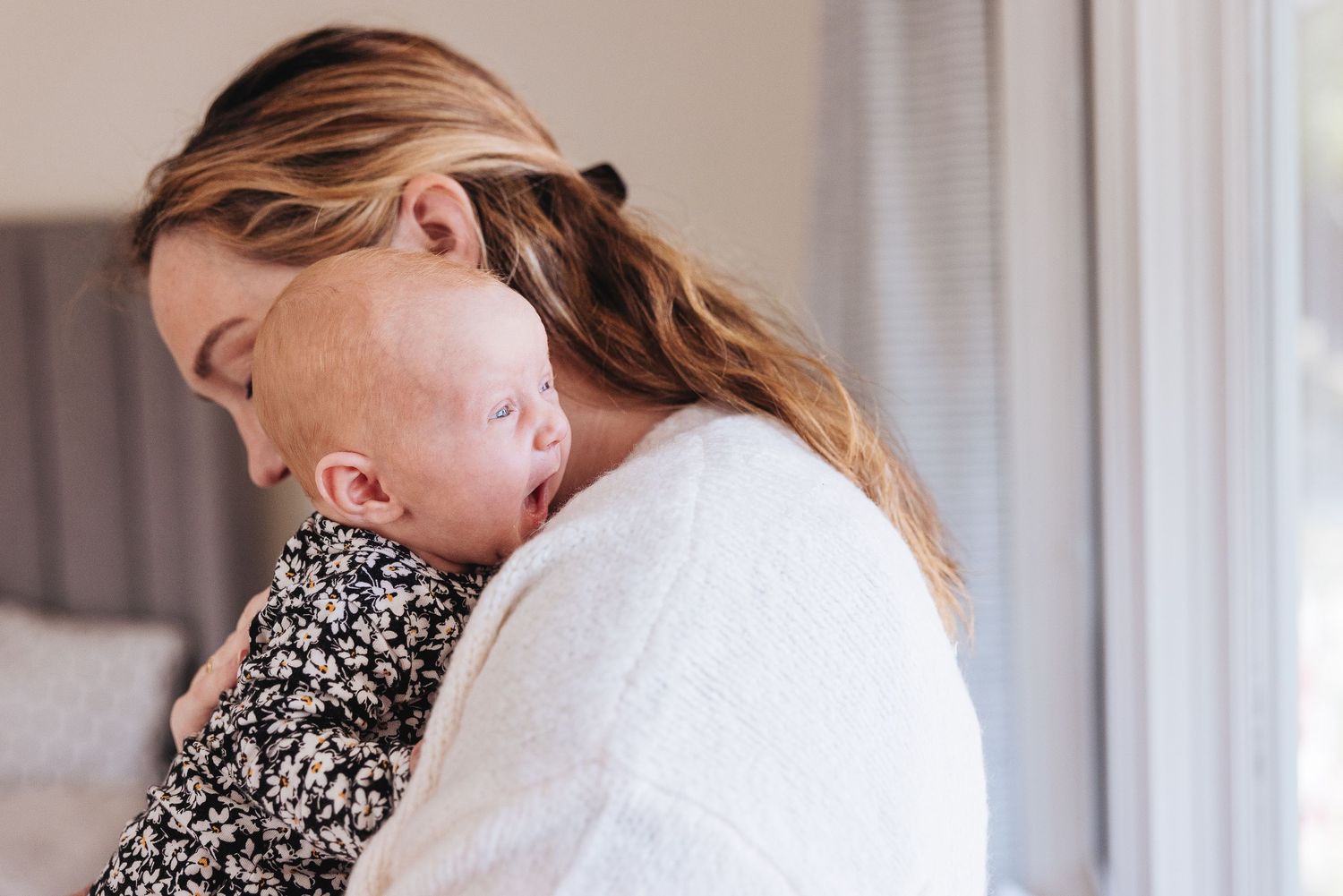A tender moment of a baby sleeping on someone's shoulder wearing a floral print outfit.