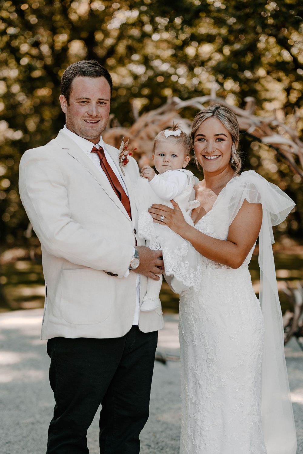 Wedding party in white attire posing outdoors with trees in background.