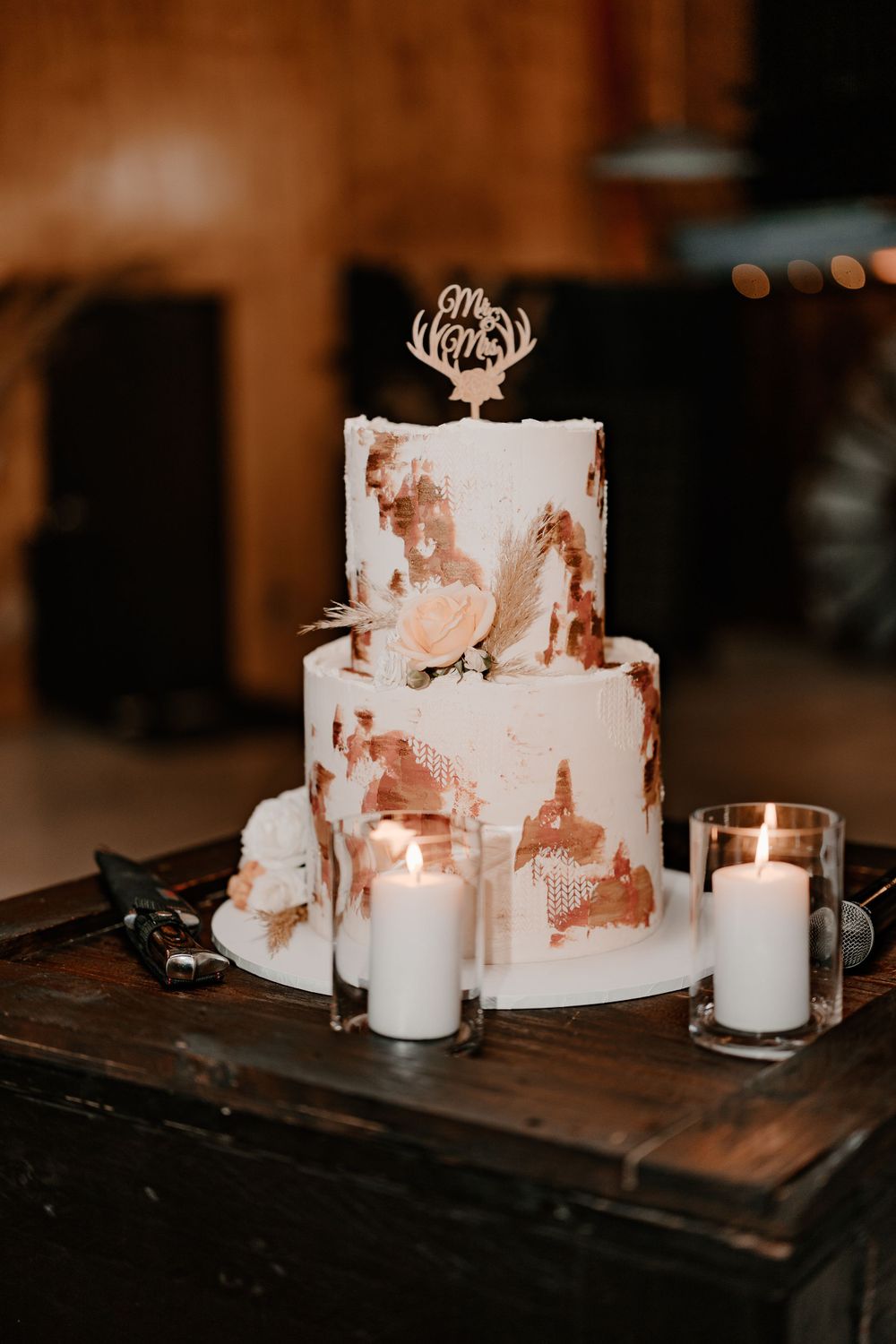 Modern white wedding cake with rustic design elements and lit candles on wooden table.