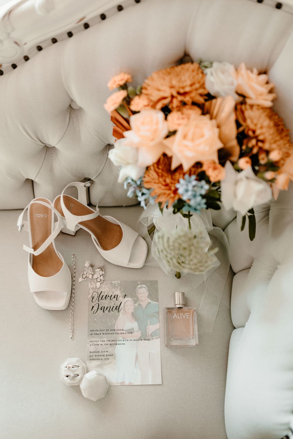Wedding details styled on white tufted chair with peach florals, white shoes and invitation.