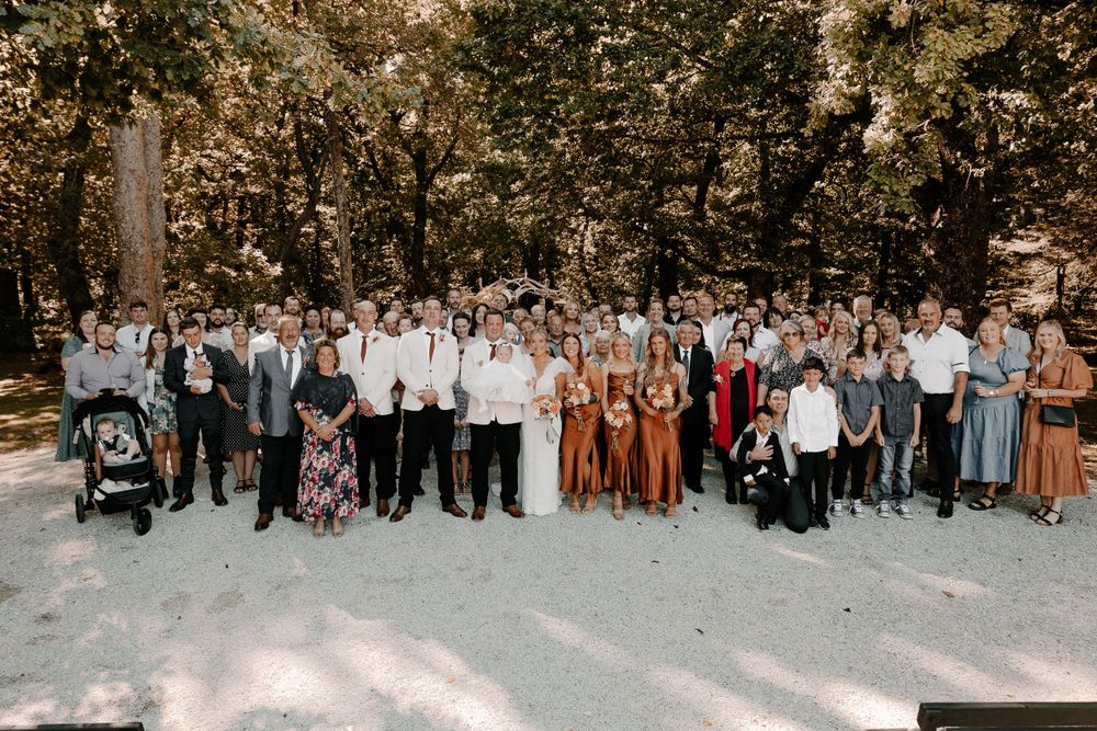 Large wedding group photo with guests arranged in rows outdoors.