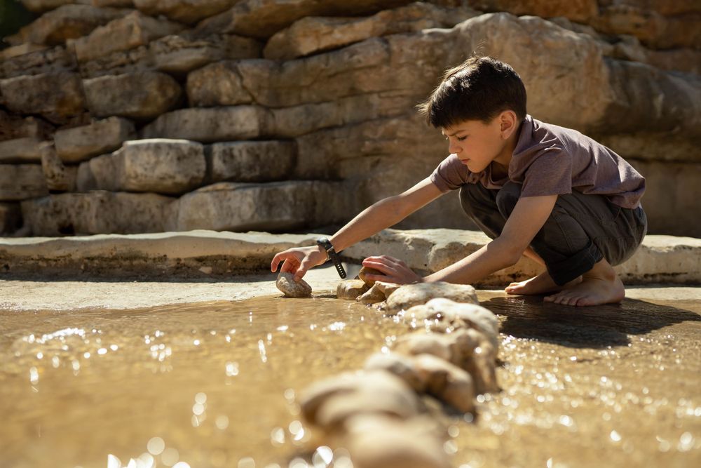 young boy stacking rocks in water