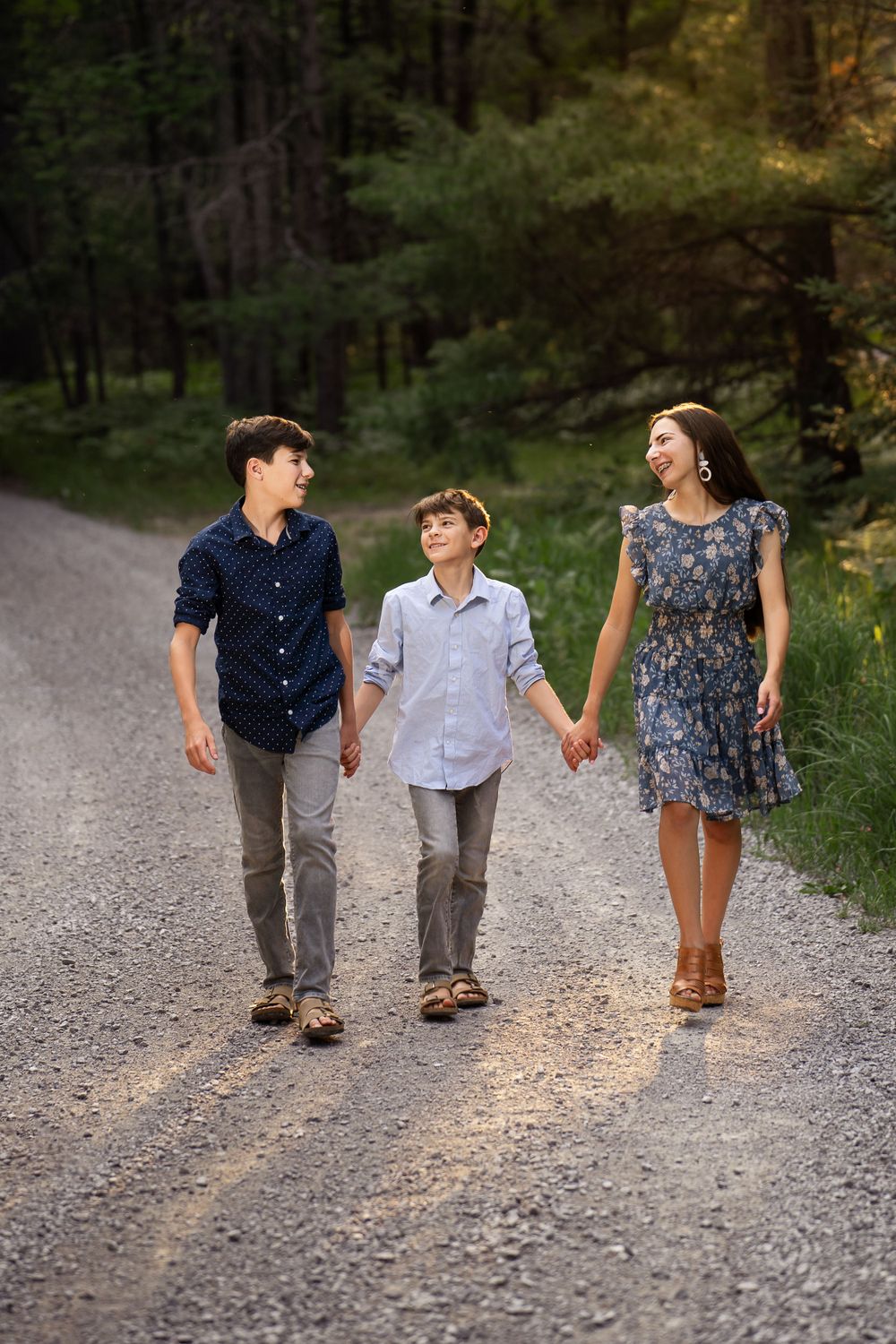teenage girl wearing blue dress holding hands with brother wearing light blue shirt and teenage brother wearing navy shi