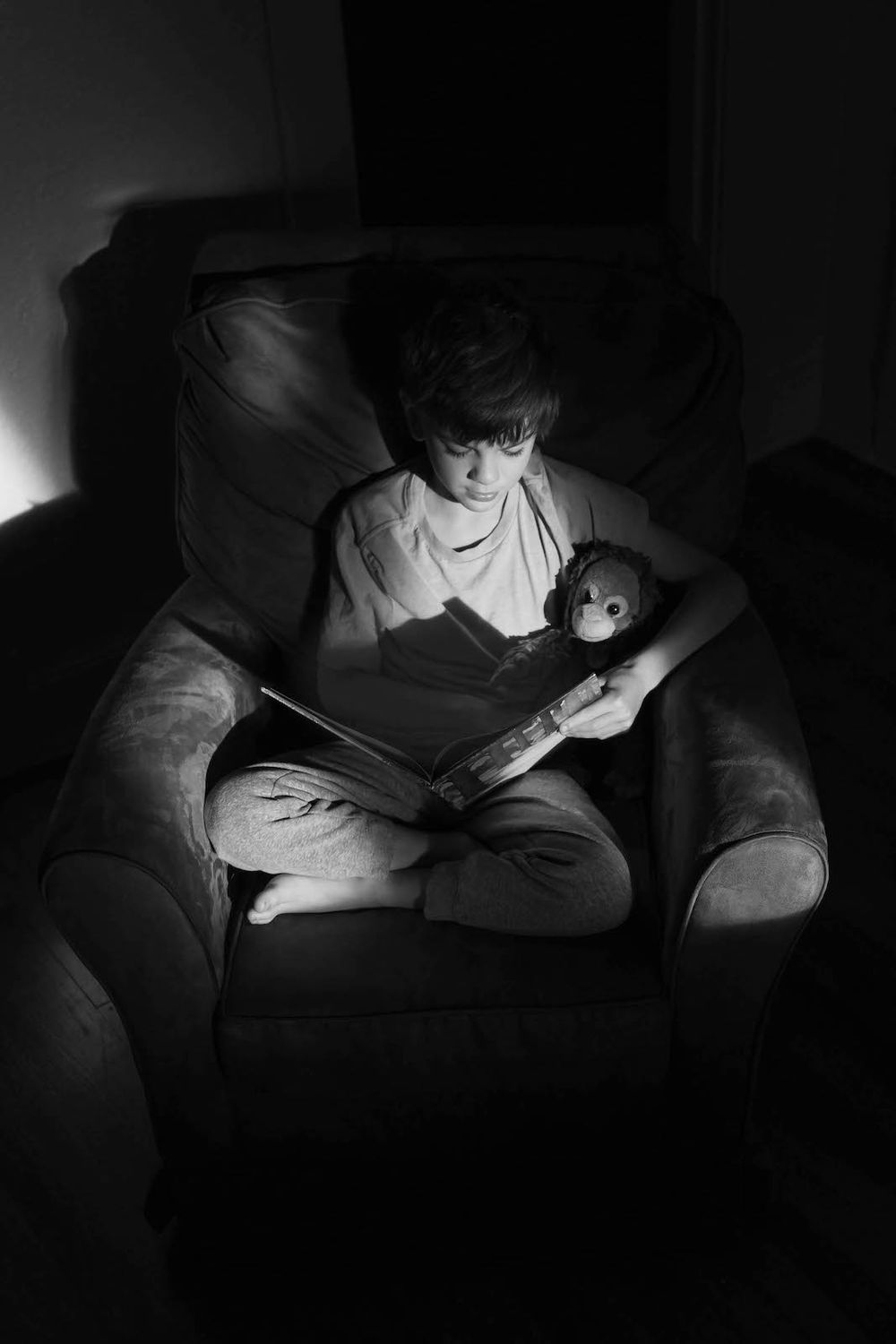 young boy sitting in chair with stuffed chimpanzee reading a bool