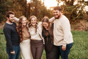 Multi-generational family group laughing in a field during a fall photo session in the Ozarks with L. Ballenger Photography.