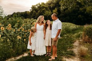 Family of five in coordinating white outfits for a summer photo session in a Branson sunflower field with L. Ballenger Photography.