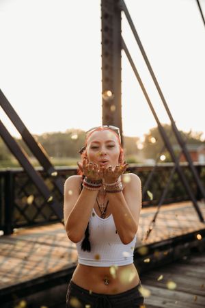 Creative senior photo session on a rustic bridge in Branson featuring a girl blowing gold glitter by L. Ballenger Photography.