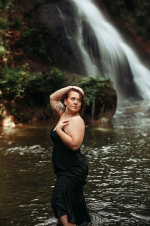 Empowering portrait of a woman in a black dress posing in front of a Branson waterfall, captured by L. Ballenger Photography.
