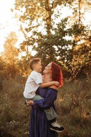 Mother lifting her son in a golden hour field during a motherhood photo session with L. Ballenger Photography.