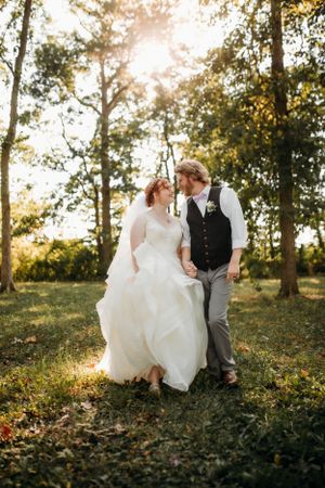 Bride and groom walking through a sun-drenched forest captured by Branson, MO Photographer L. Ballenger Photography.