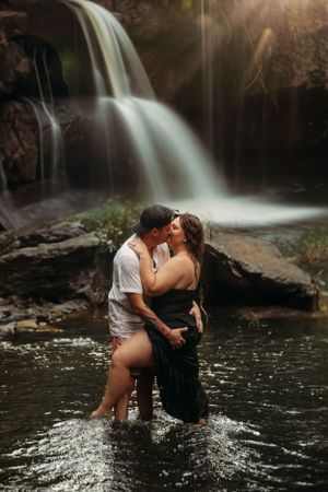 Romantic couple embracing in front of a waterfall during a sunset photo session in Branson, MO by L. Ballenger Photography.