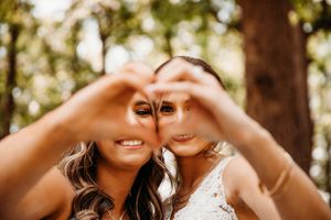 A bride and Maid of Honor making a heart shape with their hands during a fun wedding photo session in Branson by L. Ballenger Photography.