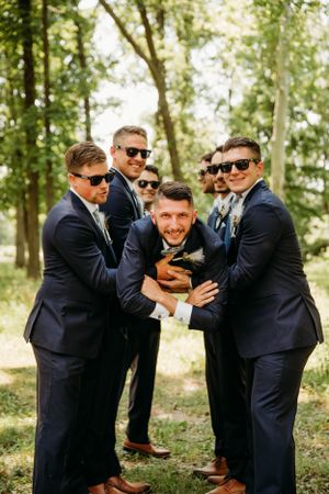 Fun groomsmen portrait in a forest setting featuring navy suits, captured by Branson, MO Photographer L. Ballenger Photography.