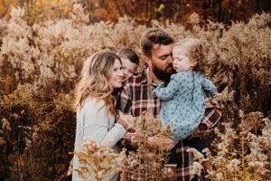 Family of three sitting in tall autumn grass for a cozy fall photo session in the Ozark Mountains with L. Ballenger Photography.