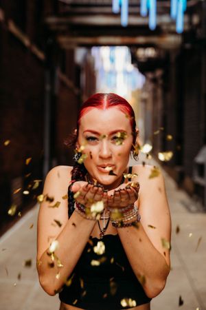 Creative urban senior portrait featuring a girl blowing gold glitter, captured by L. Ballenger Photography in Branson, Mo.