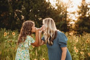 A mother and daughter sharing a sweet moment in a sun-drenched field during a photo session in Branson, Mo with L. Ballenger Photography.