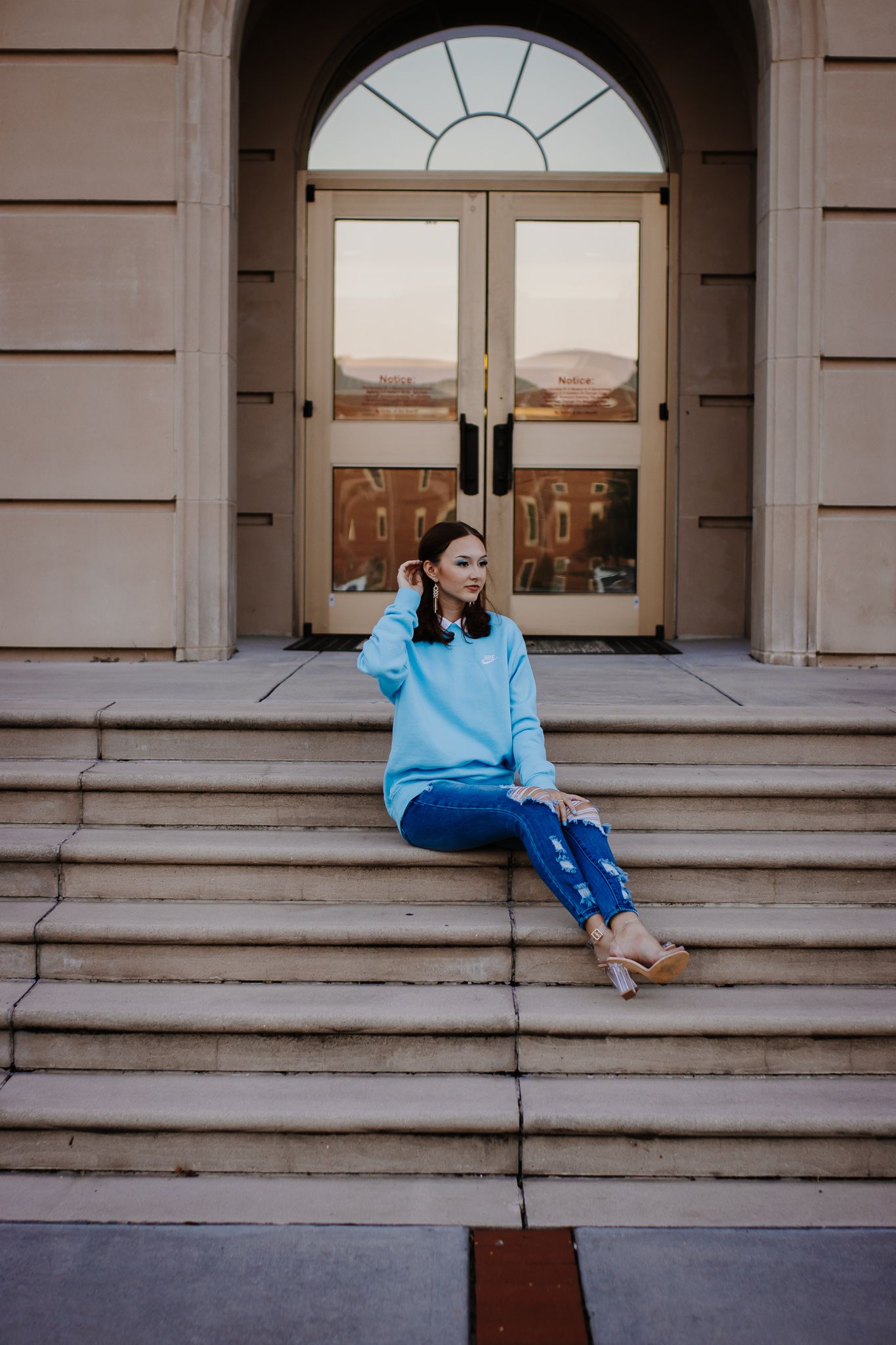 Someone in bright blue sweater sits casually on stone steps in front of arched doorway.
